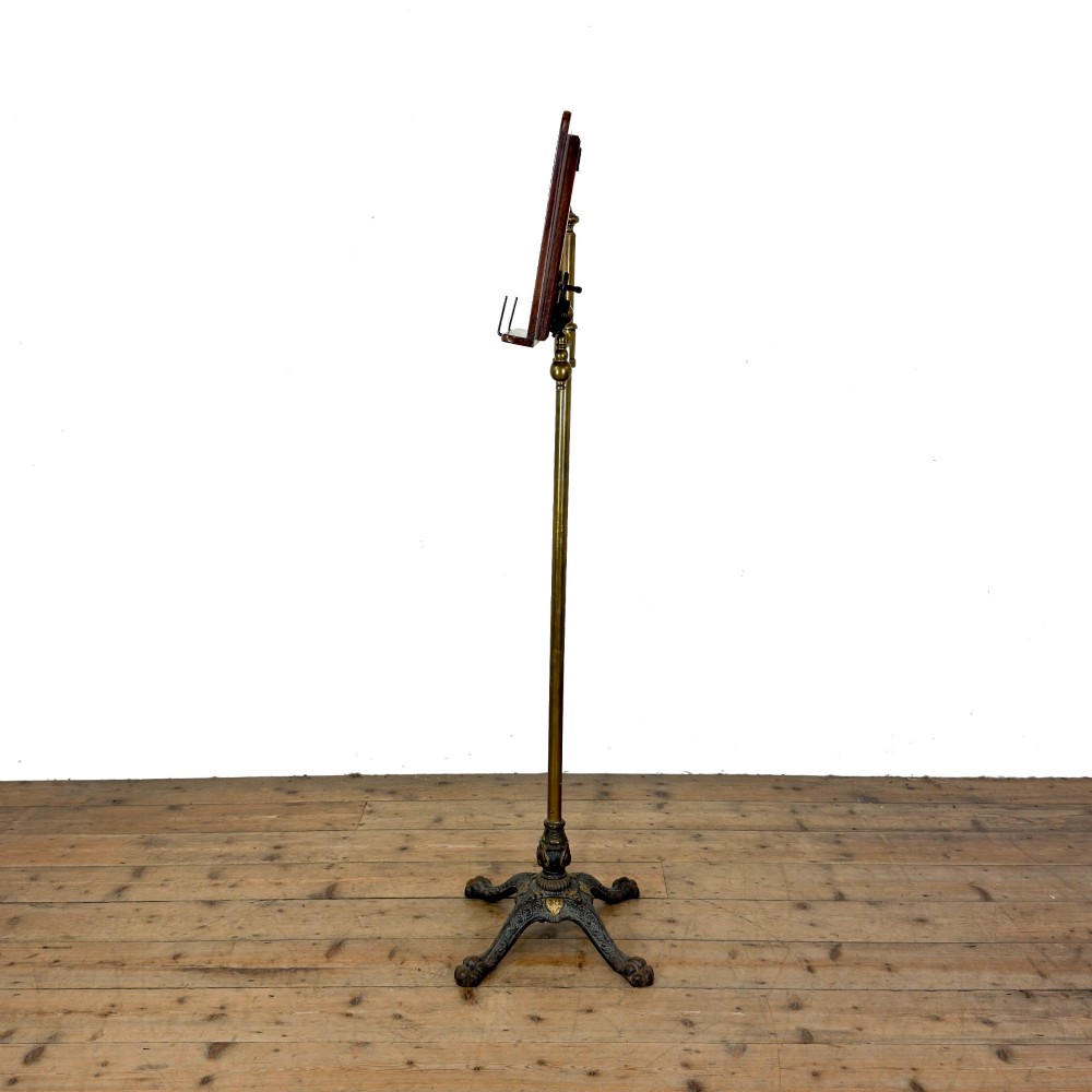 A Victorian adjustable reading stand featuring a cast iron decorative base, a brass column with an articulated swing arm, and a rectangular mahogany book rest. View VII