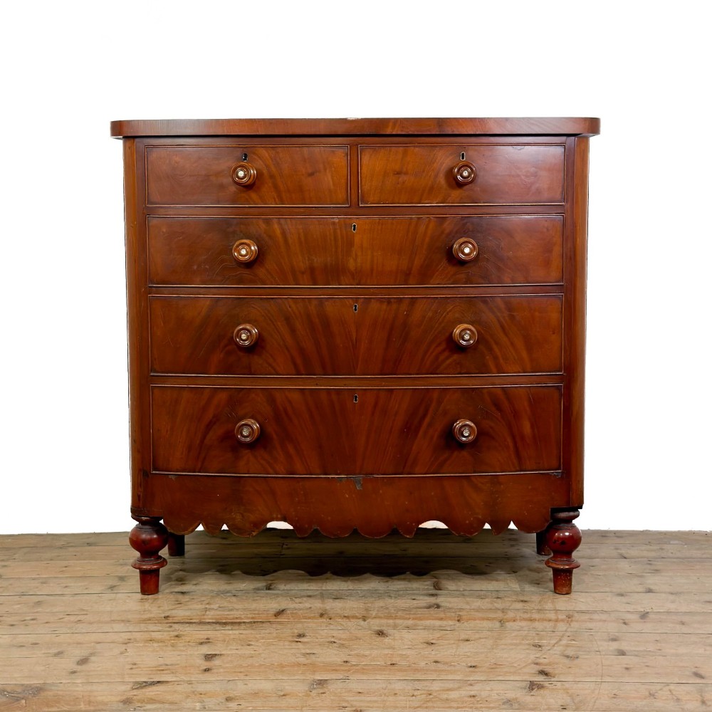 A Victorian mahogany chest of drawers featuring two short drawers over three long drawers with turned wooden knobs and a scalloped lower apron.