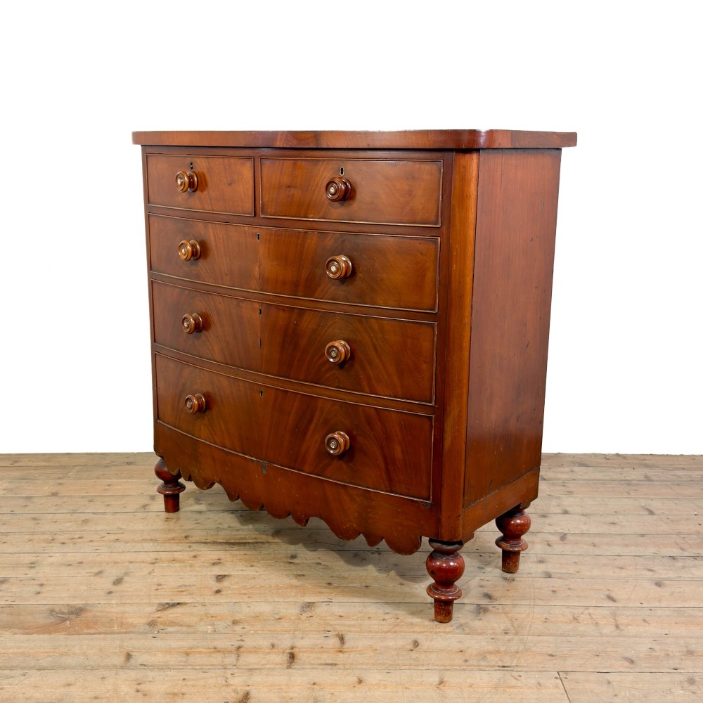 A Victorian mahogany chest of drawers featuring two short drawers over three long drawers with turned wooden knobs and a scalloped lower apron. View IV