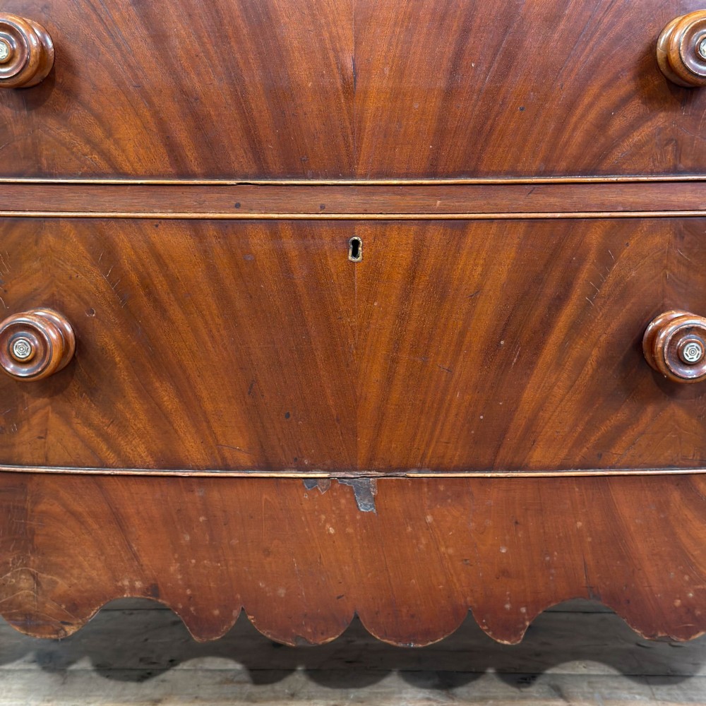 A Victorian mahogany chest of drawers featuring two short drawers over three long drawers with turned wooden knobs and a scalloped lower apron. View VI