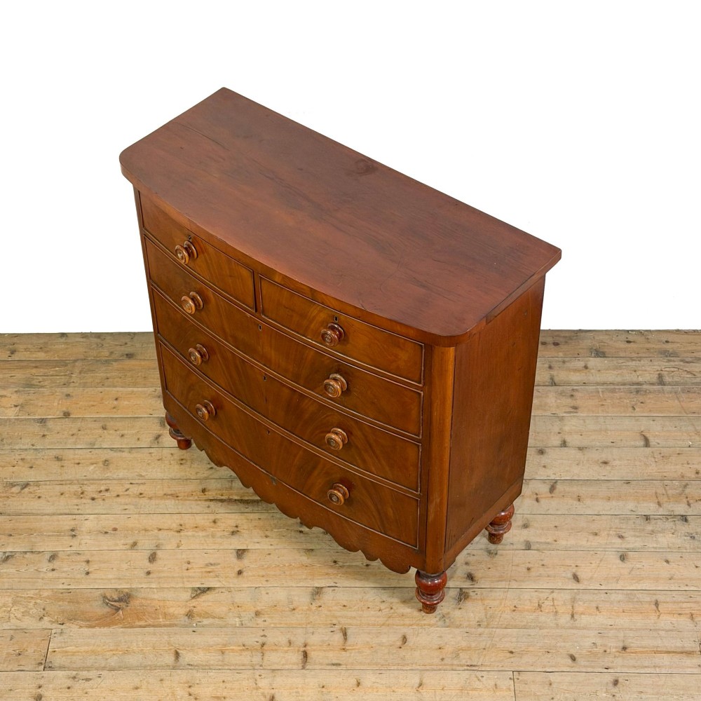 A Victorian mahogany chest of drawers featuring two short drawers over three long drawers with turned wooden knobs and a scalloped lower apron. View VII