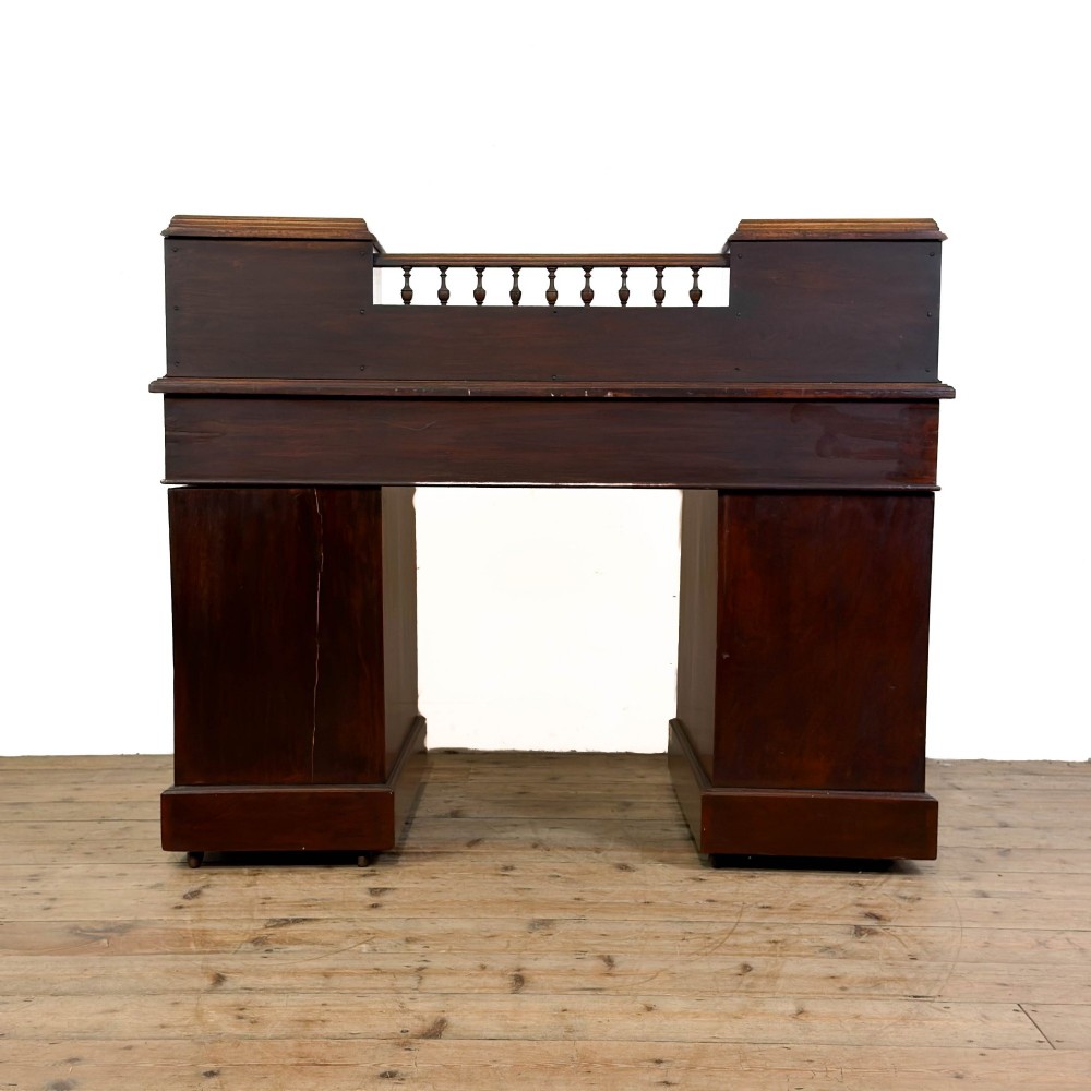 An antique Victorian mahogany pedestal desk featuring a raised gallery superstructure, multiple drawers, and brass handles. View VI