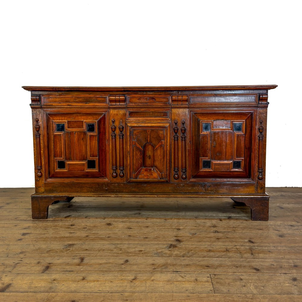 A seventeenth-century style carved oak coffer featuring geometric panelling, split baluster turnings, and dark square inlay details on a plinth base.