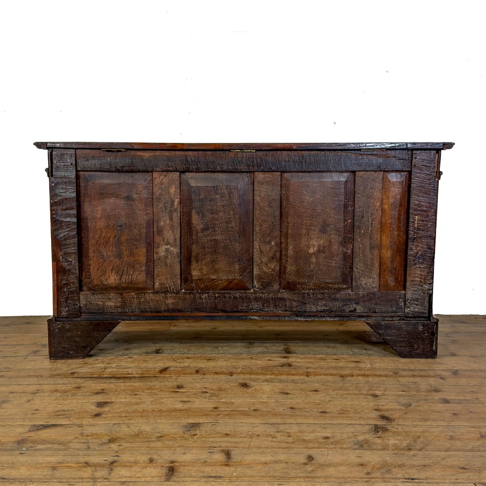 A seventeenth-century style carved oak coffer featuring geometric panelling, split baluster turnings, and dark square inlay details on a plinth base. View VI