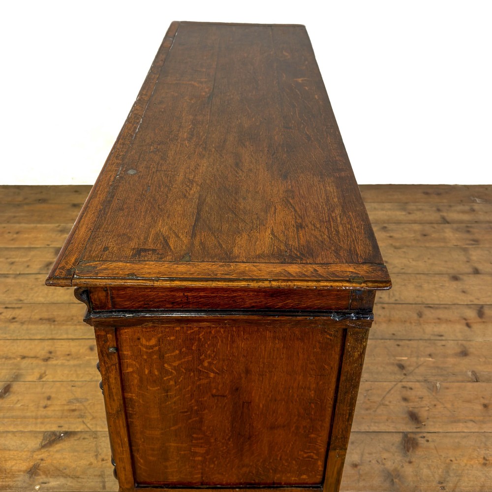 A seventeenth-century style carved oak coffer featuring geometric panelling, split baluster turnings, and dark square inlay details on a plinth base. View IX