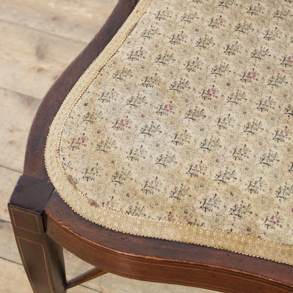 An antique Edwardian mahogany corner armchair featuring inlaid marquetry oval patera, two pierced back splats, tapered legs, and a patterned fabric seat. View VI