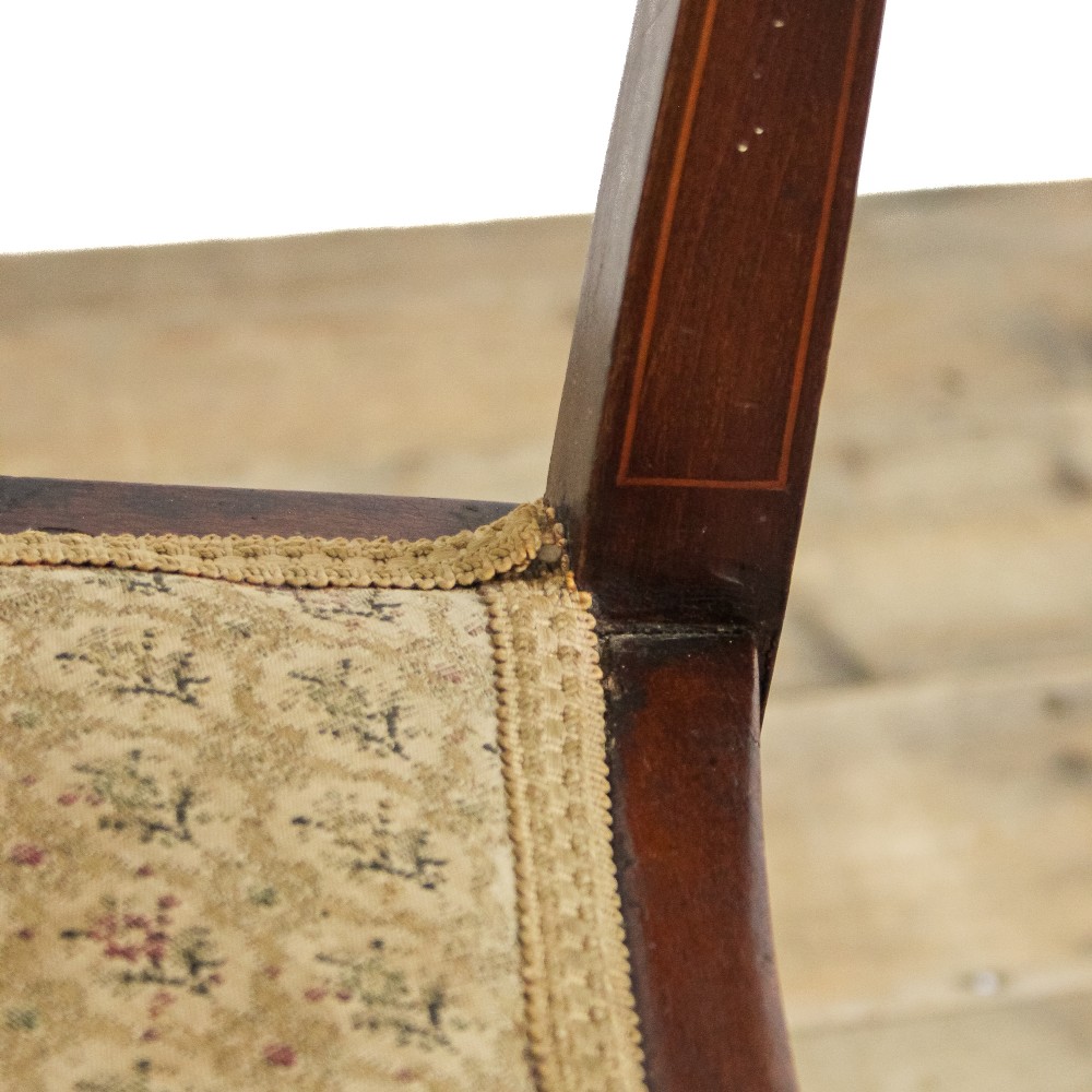 An antique Edwardian mahogany corner armchair featuring inlaid marquetry oval patera, two pierced back splats, tapered legs, and a patterned fabric seat. View IX