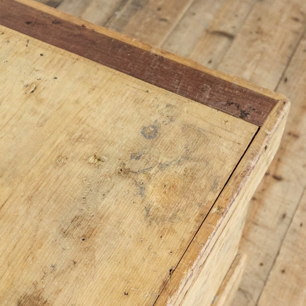A rectangular natural pine storage chest featuring visible hand-cut dovetail joinery, a fitted flat lid, a central keyhole escutcheon, and a thick timber plinth base. View VI