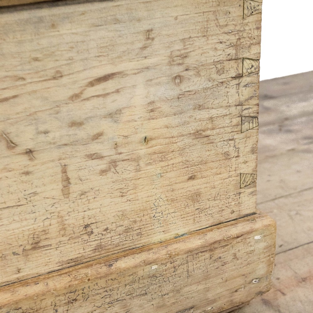 A rectangular natural pine storage chest featuring visible hand-cut dovetail joinery, a fitted flat lid, a central keyhole escutcheon, and a thick timber plinth base. View X