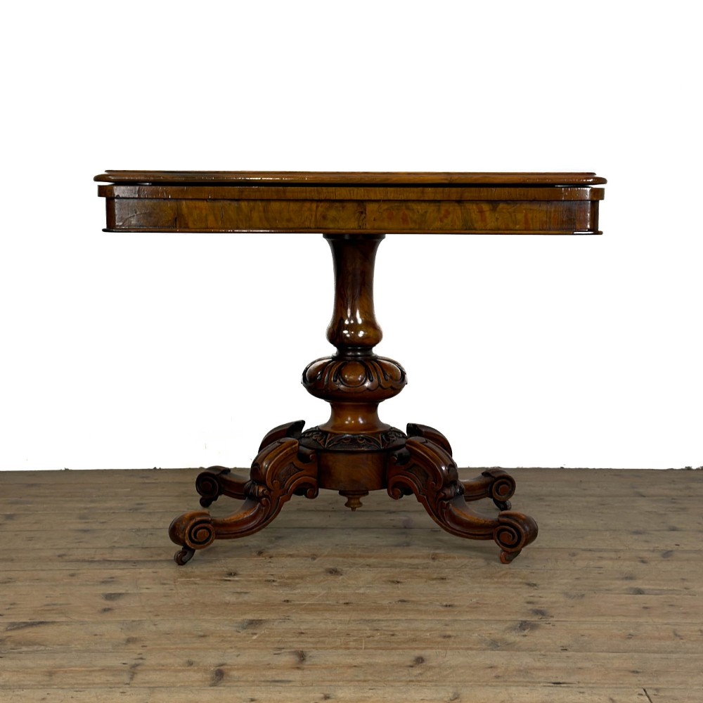 An antique Victorian walnut foldover card table featuring a rectangular swivel top, turned central column, and carved scroll feet.