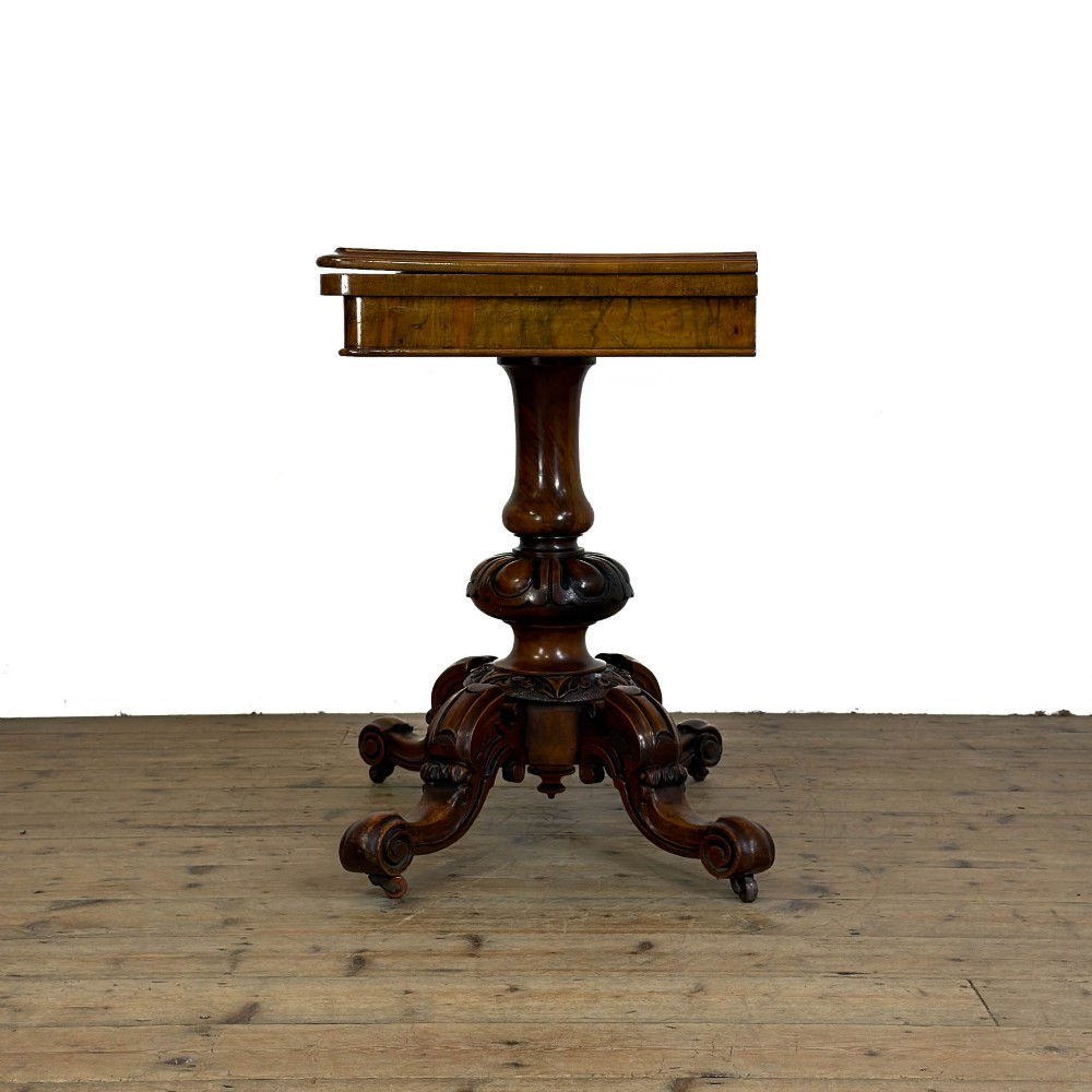 An antique Victorian walnut foldover card table featuring a rectangular swivel top, turned central column, and carved scroll feet. View V