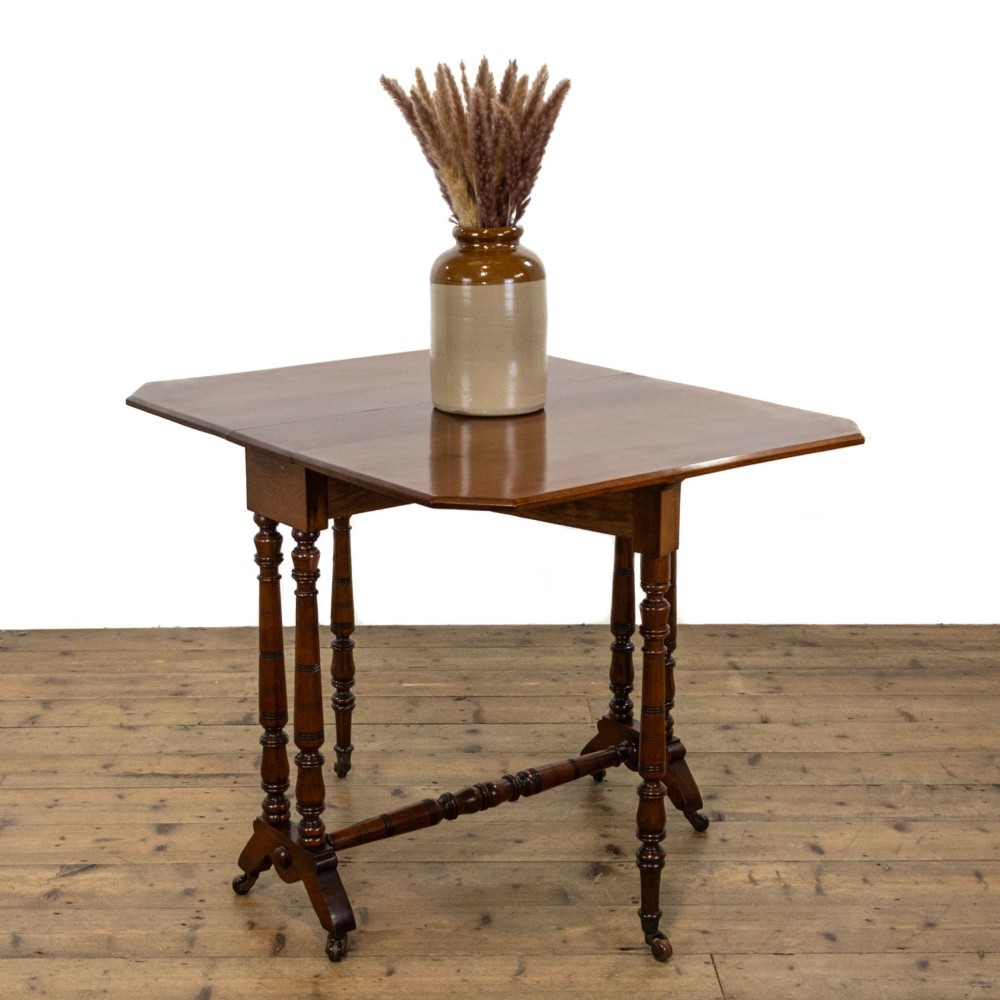 An antique Victorian walnut Sutherland table featuring turned legs, a drop-leaf top, a cross stretcher, and small castors.