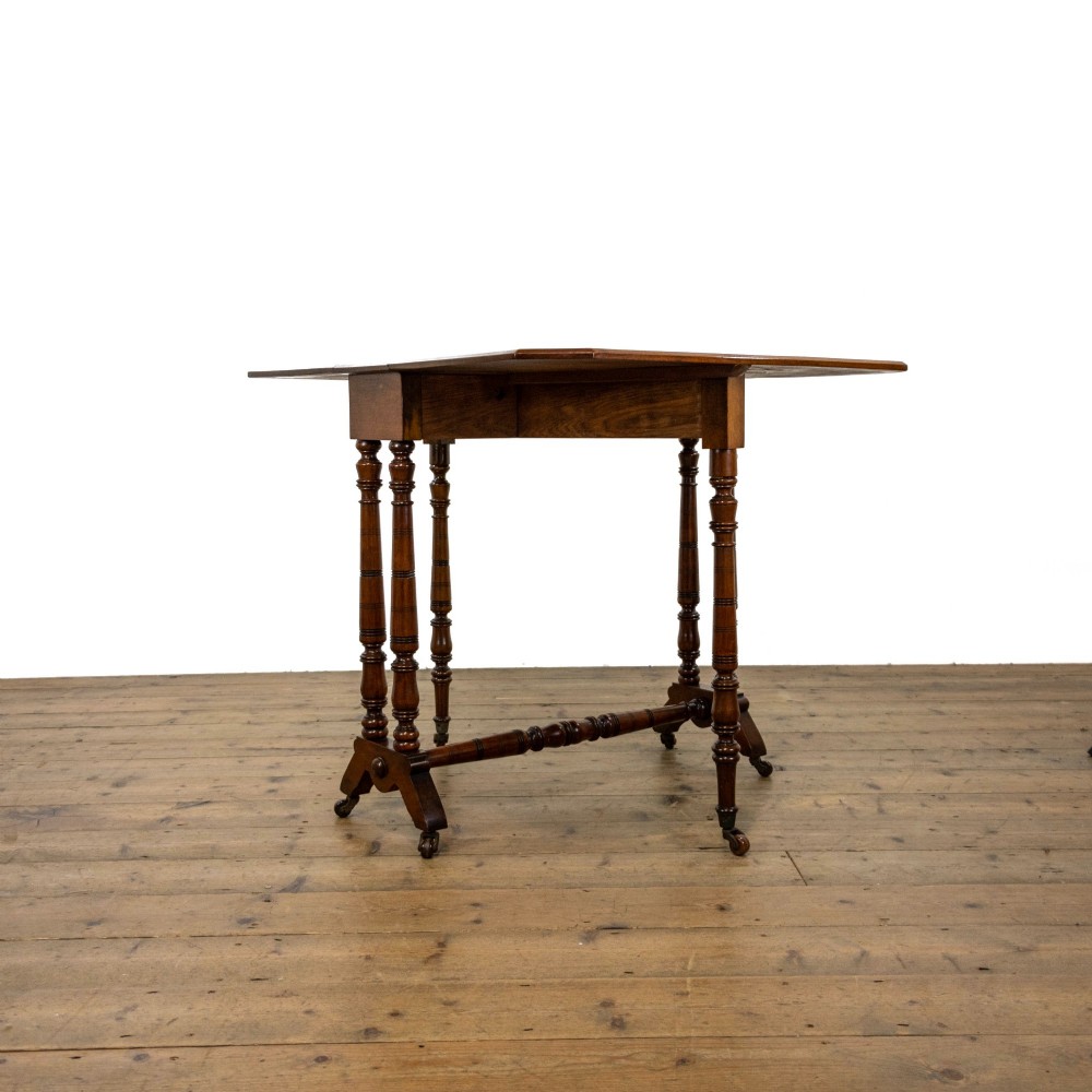 An antique Victorian walnut Sutherland table featuring turned legs, a drop-leaf top, a cross stretcher, and small castors. View III