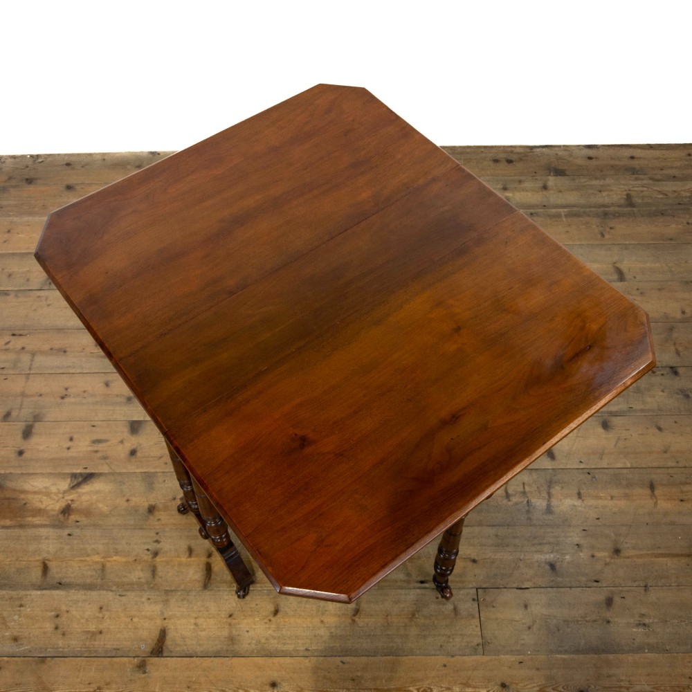 An antique Victorian walnut Sutherland table featuring turned legs, a drop-leaf top, a cross stretcher, and small castors. View IV