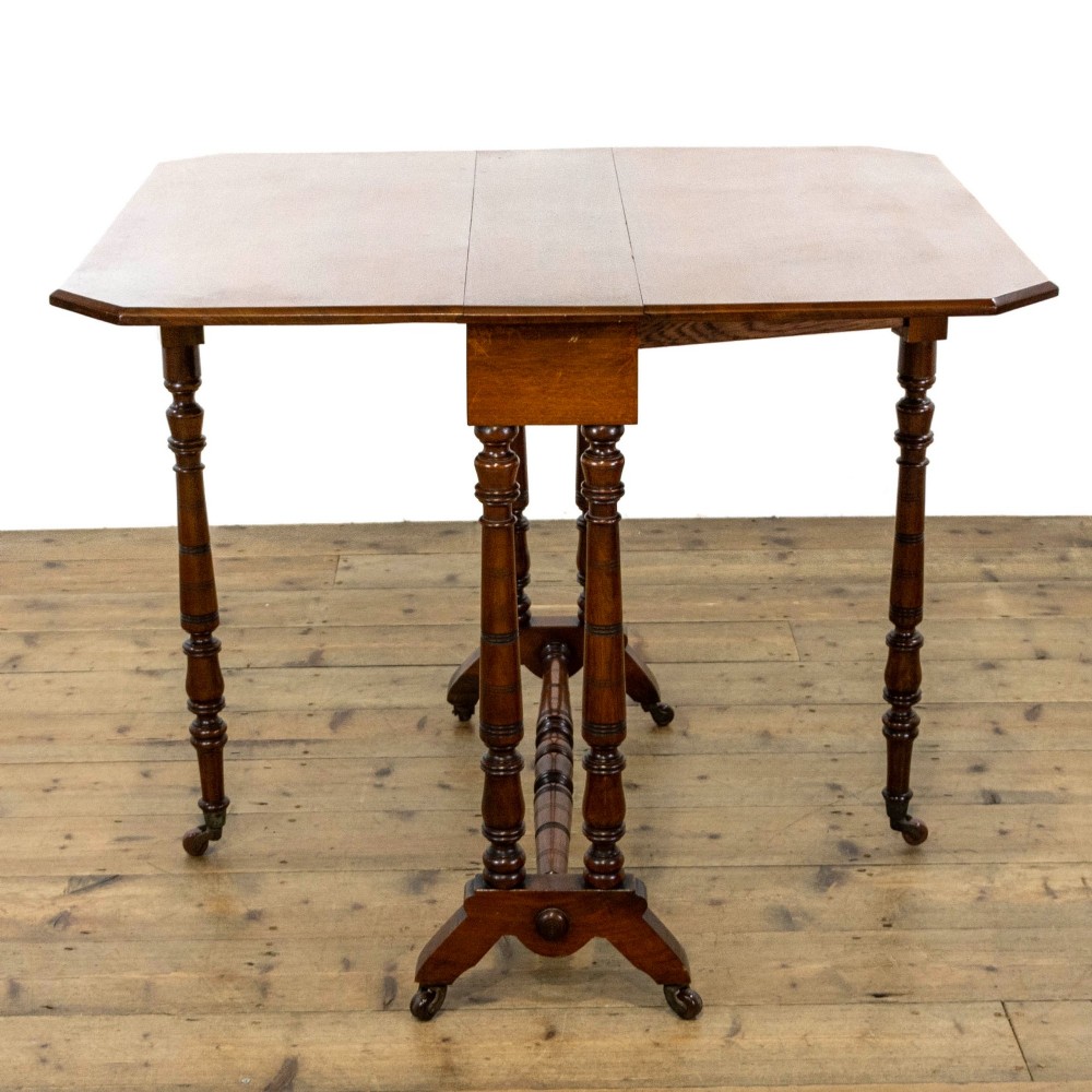 An antique Victorian walnut Sutherland table featuring turned legs, a drop-leaf top, a cross stretcher, and small castors. View V