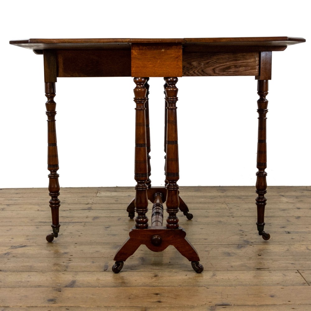 An antique Victorian walnut Sutherland table featuring turned legs, a drop-leaf top, a cross stretcher, and small castors. View VI