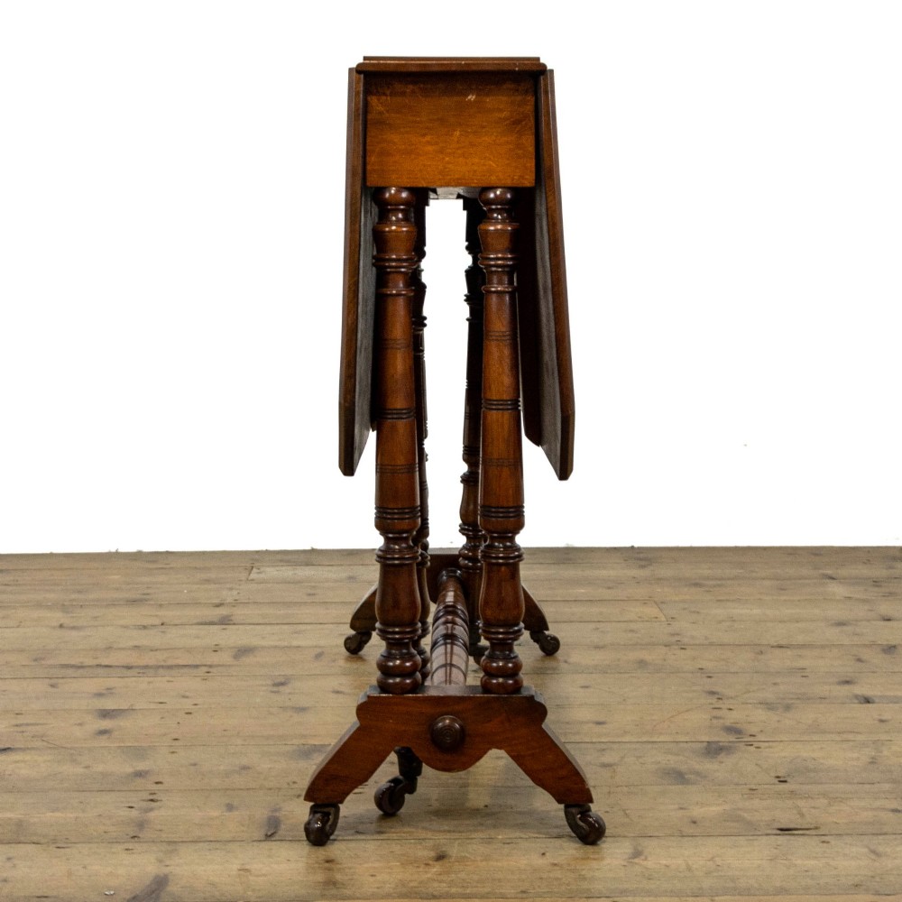 An antique Victorian walnut Sutherland table featuring turned legs, a drop-leaf top, a cross stretcher, and small castors. View VII