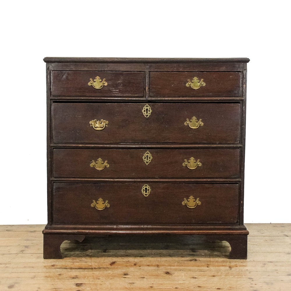 An eighteenth-century dark oak chest of drawers featuring a two-over-three drawer configuration, brass swan-neck handles, decorative keyhole escutcheons, and shaped bracket feet.