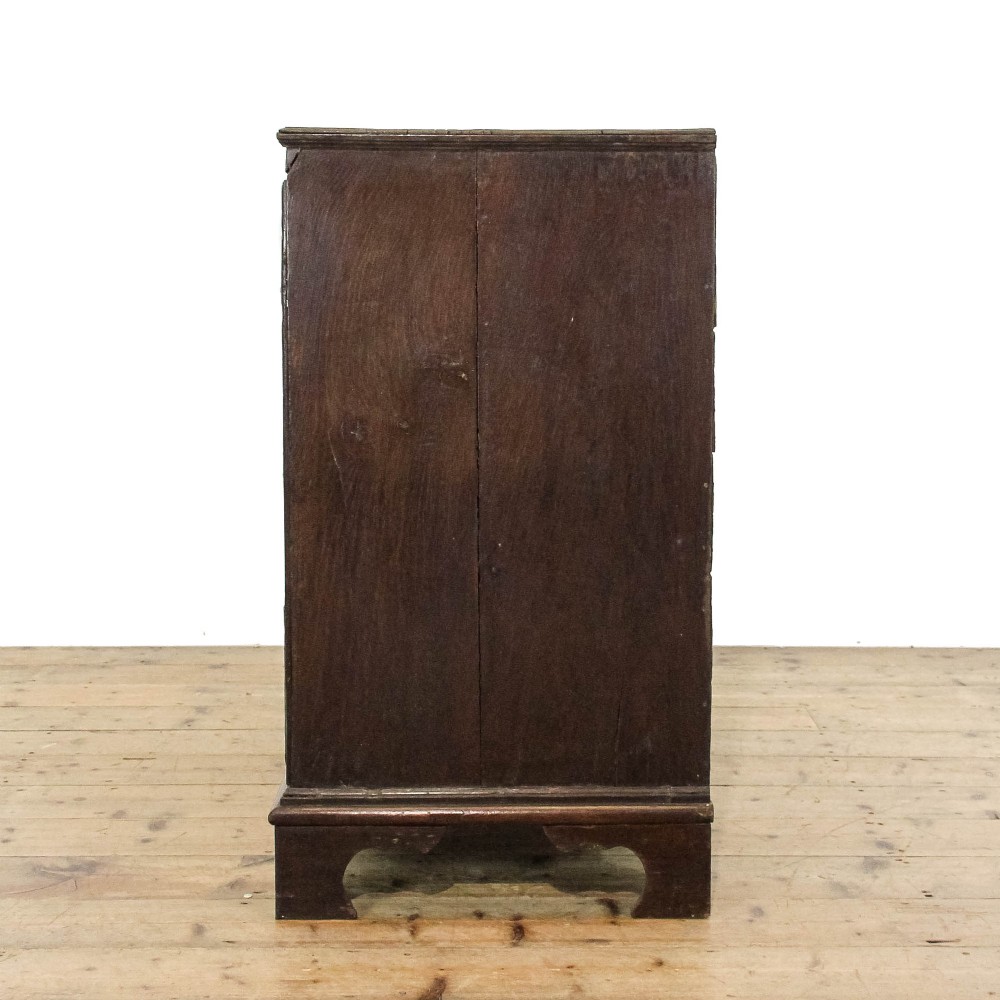 An eighteenth-century dark oak chest of drawers featuring a two-over-three drawer configuration, brass swan-neck handles, decorative keyhole escutcheons, and shaped bracket feet. View V