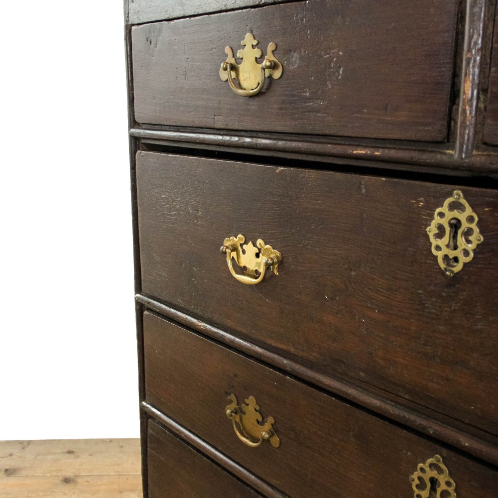 An eighteenth-century dark oak chest of drawers featuring a two-over-three drawer configuration, brass swan-neck handles, decorative keyhole escutcheons, and shaped bracket feet. View X