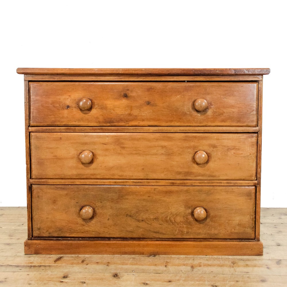 An antique pine chest of drawers featuring three wide drawers with turned wooden knob handles and a low plinth base.