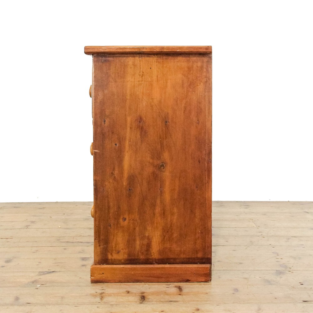 An antique pine chest of drawers featuring three wide drawers with turned wooden knob handles and a low plinth base. View V