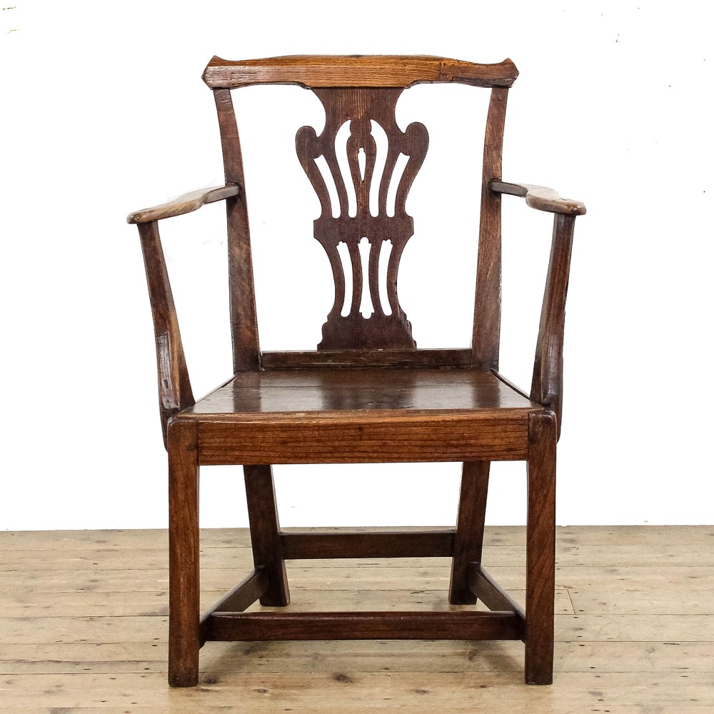 A George III period oak open armchair featuring a pierced vase-shaped back splat, swept arms, a solid wooden seat, and square legs joined by stretchers.