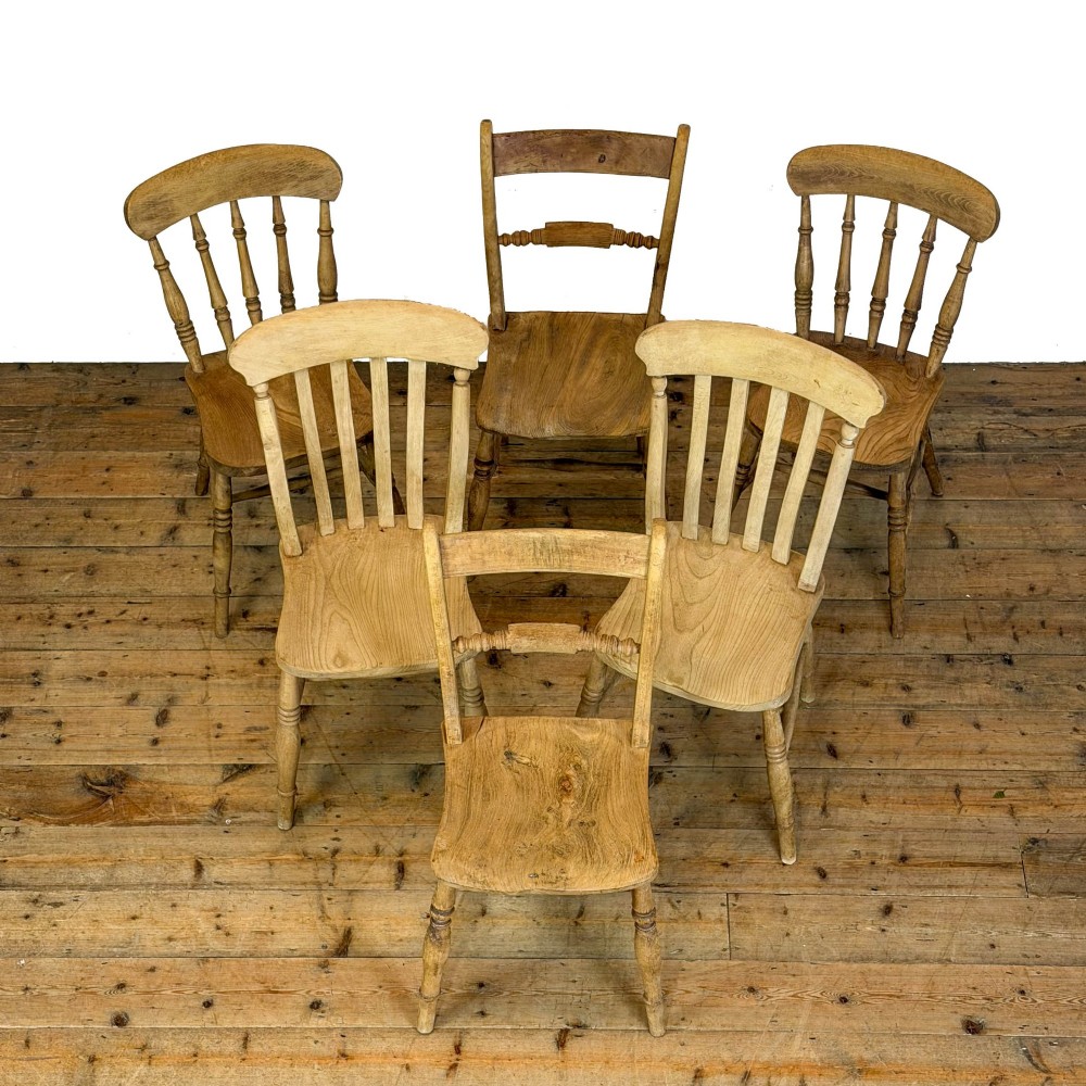 A set of six mismatched vintage wooden dining chairs with turned legs and varied slat and spindle backs arranged together. View II