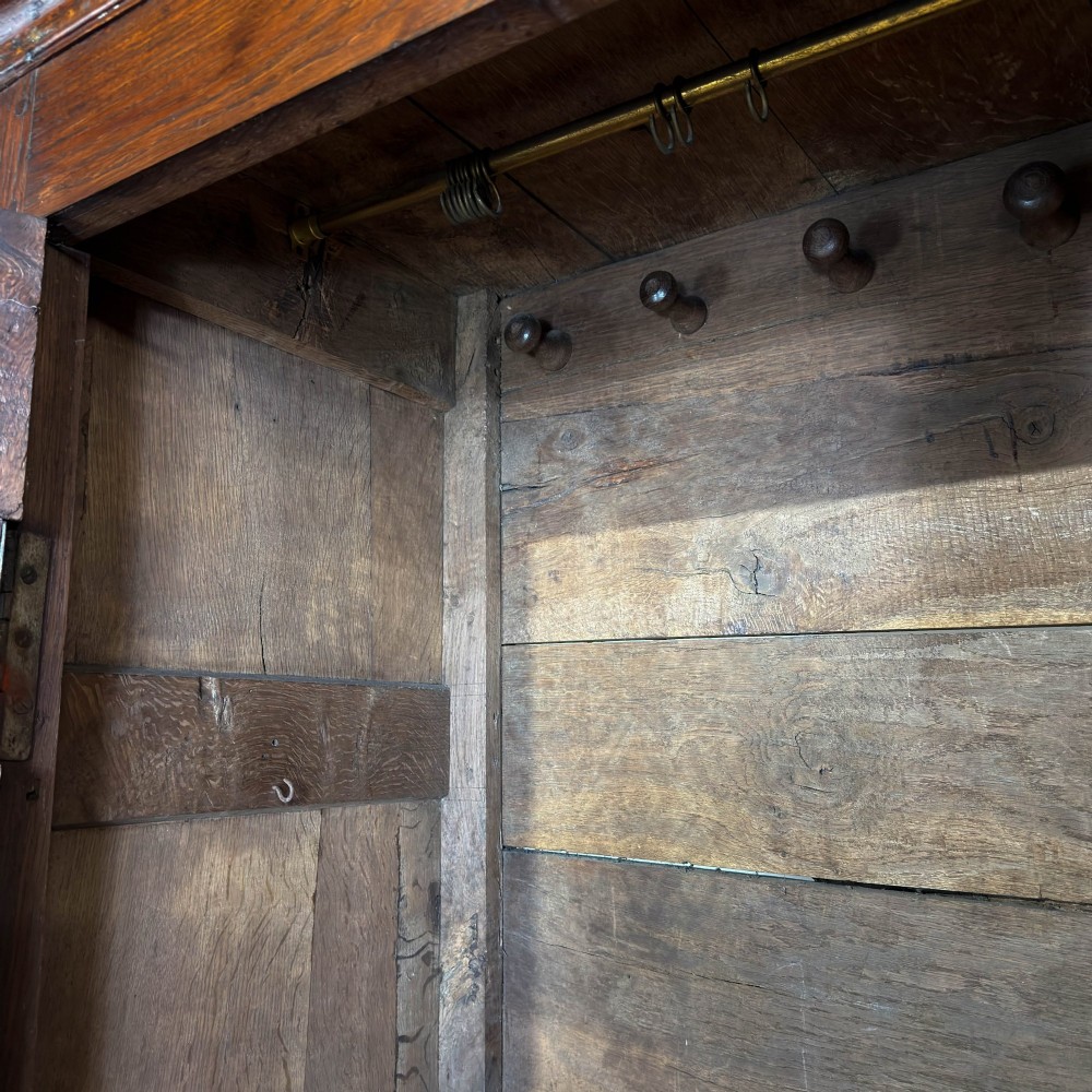 An eighteenth-century dark oak livery cupboard featuring double arched fielded panel doors over a lower drawer base with brass handles. View V