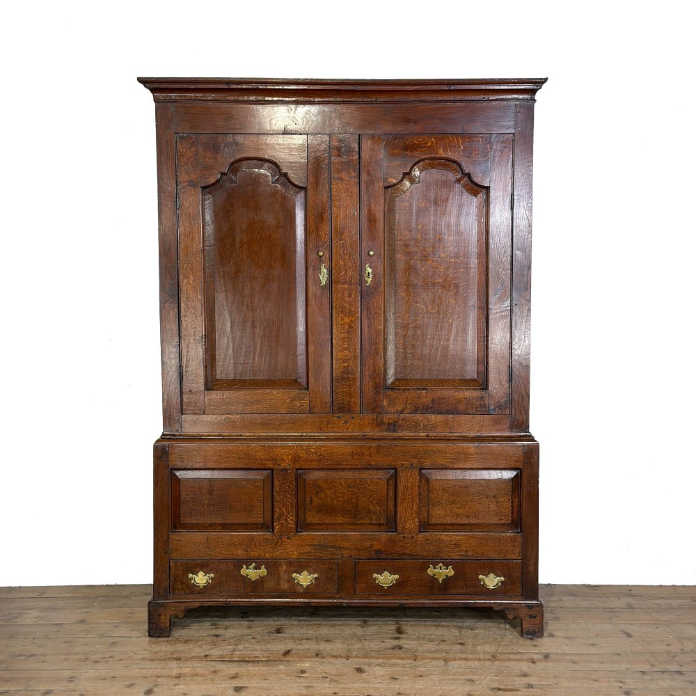 An eighteenth-century dark oak livery cupboard featuring double arched fielded panel doors over a lower drawer base with brass handles. View VI