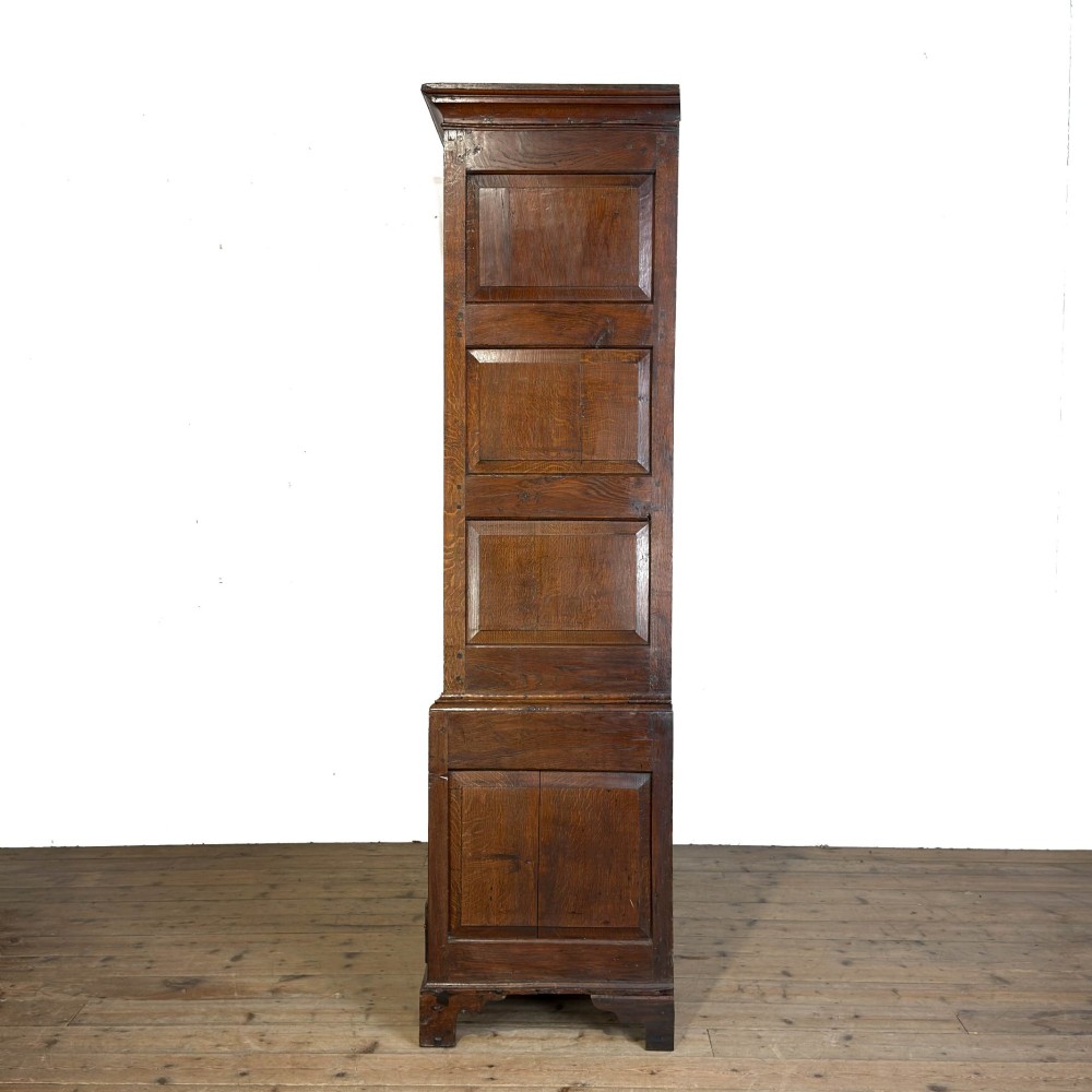 An eighteenth-century dark oak livery cupboard featuring double arched fielded panel doors over a lower drawer base with brass handles. View VIII