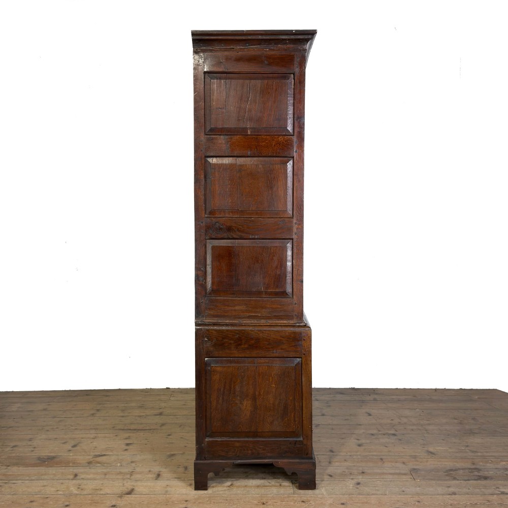 An eighteenth-century dark oak livery cupboard featuring double arched fielded panel doors over a lower drawer base with brass handles. View X