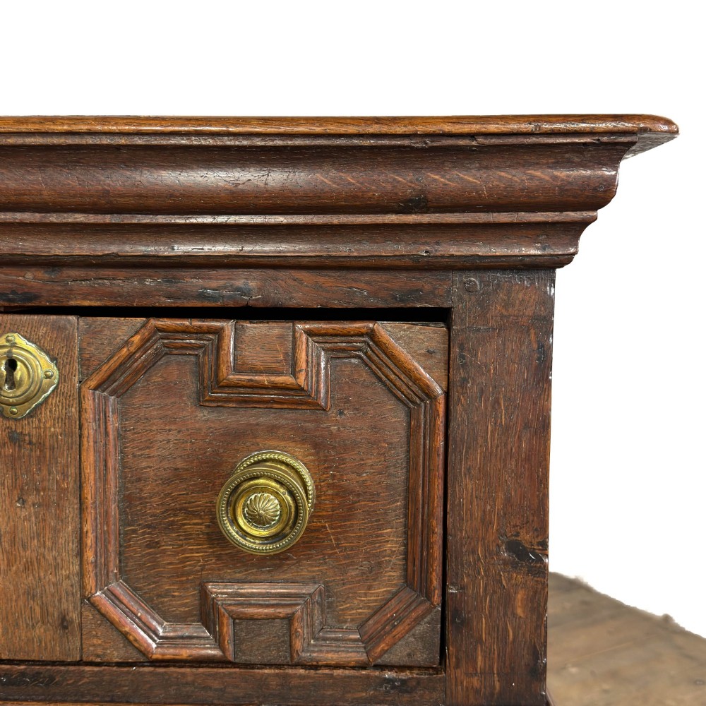 An antique dark oak dresser base featuring two drawers with geometric raised mouldings, brass handles, turned front legs, and a low stretcher. View V