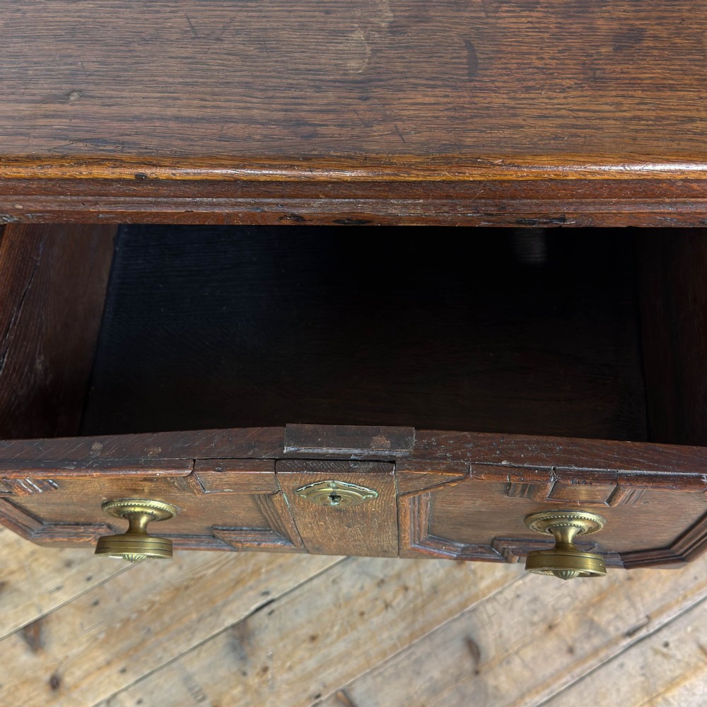 An antique dark oak dresser base featuring two drawers with geometric raised mouldings, brass handles, turned front legs, and a low stretcher. View VII