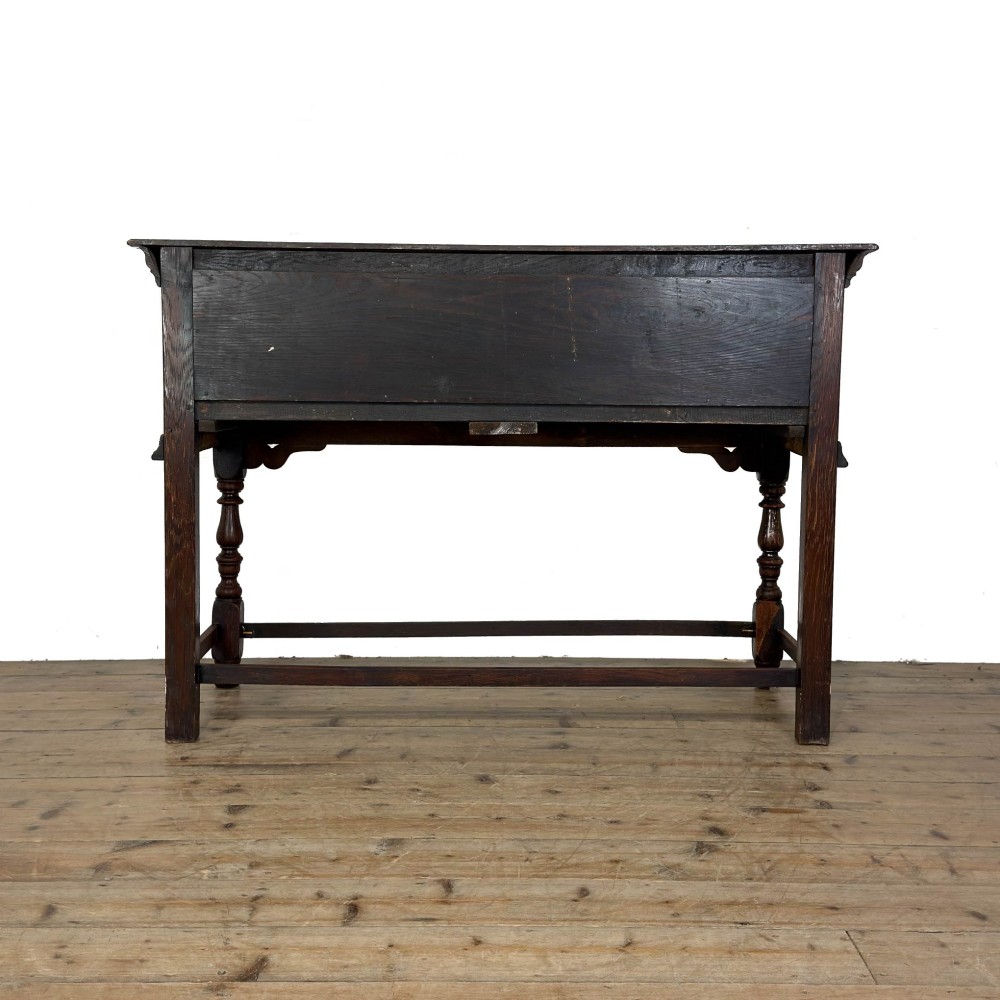 An antique dark oak dresser base featuring two drawers with geometric raised mouldings, brass handles, turned front legs, and a low stretcher. View X