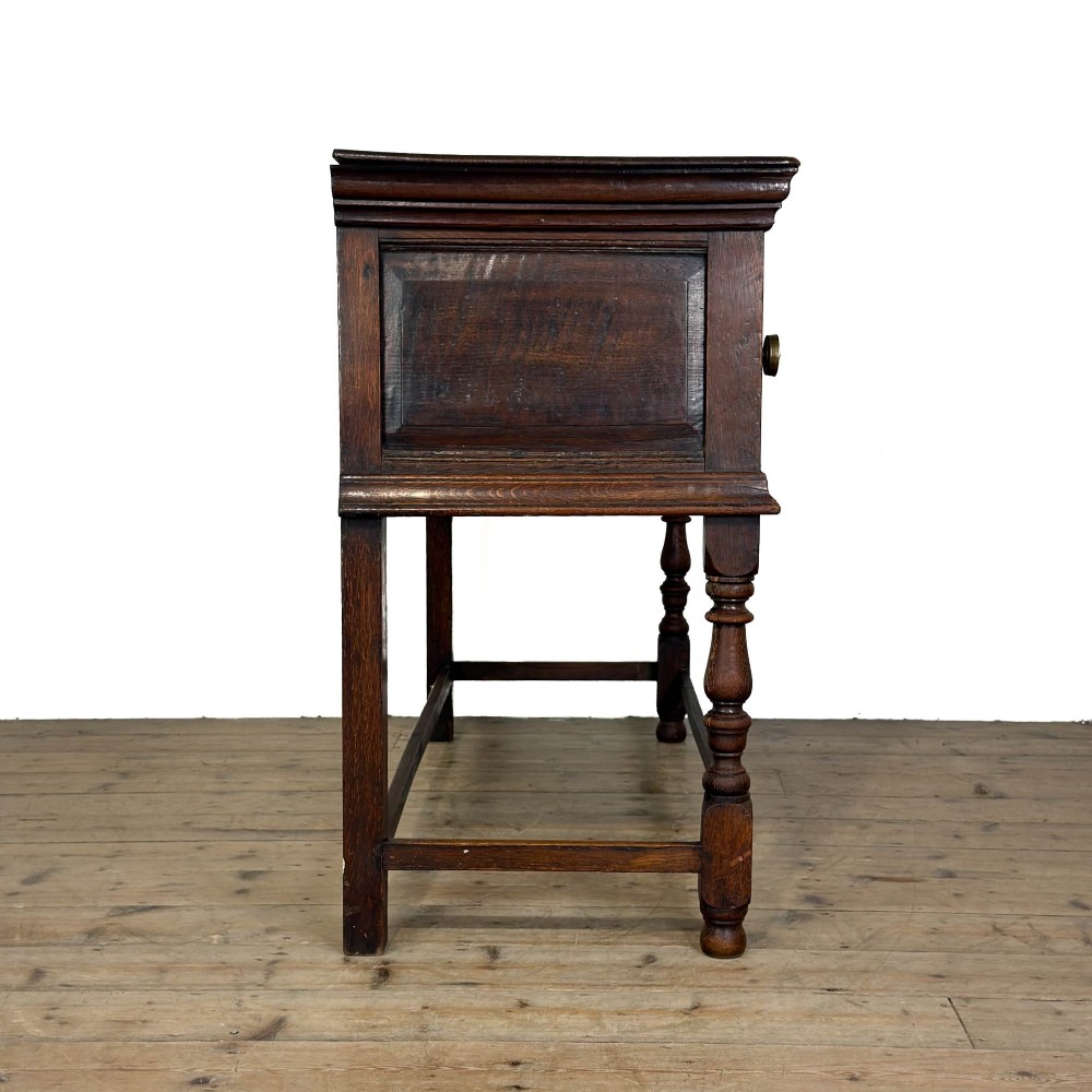 An antique dark oak dresser base featuring two drawers with geometric raised mouldings, brass handles, turned front legs, and a low stretcher. View XI