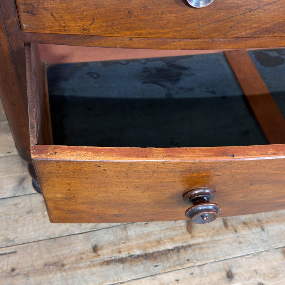 A Victorian mahogany chest of drawers featuring a bowfront profile, two short over three long graduating drawers, turned wooden knobs, and turned feet. View VIII
