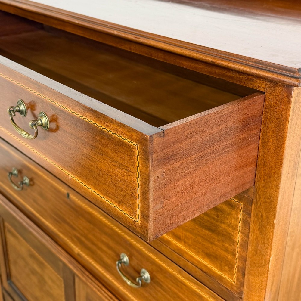 An antique Edwardian mahogany tallboy chest featuring three upper drawers above a double-door cupboard with satinwood string inlay and brass castors. View V