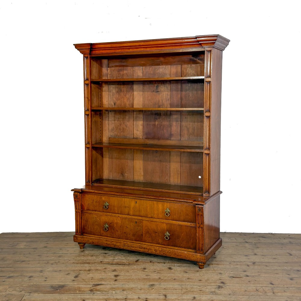 A tall antique open bookcase crafted from warm brown walnut featuring multiple open shelves, fluted side pilasters, and two lower drawers with brass drop handles. View III