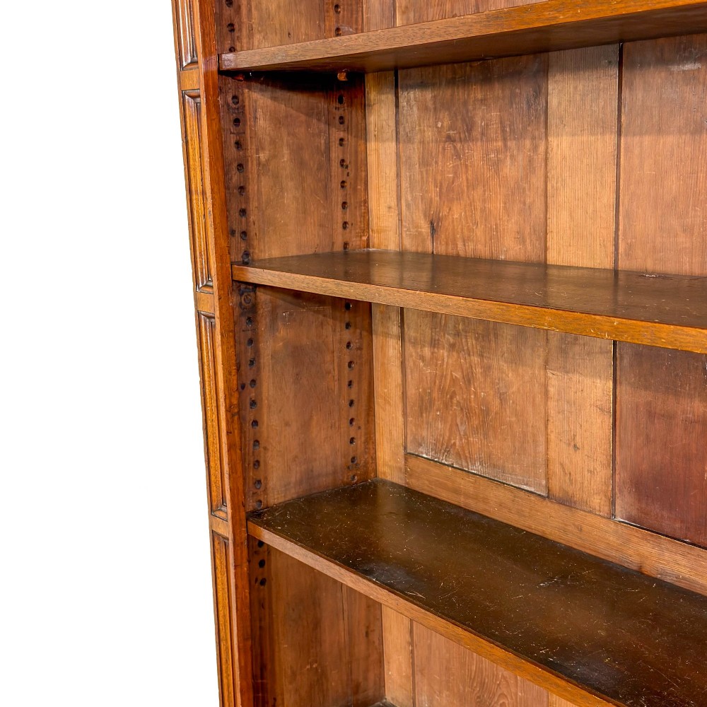 A tall antique open bookcase crafted from warm brown walnut featuring multiple open shelves, fluted side pilasters, and two lower drawers with brass drop handles. View IV