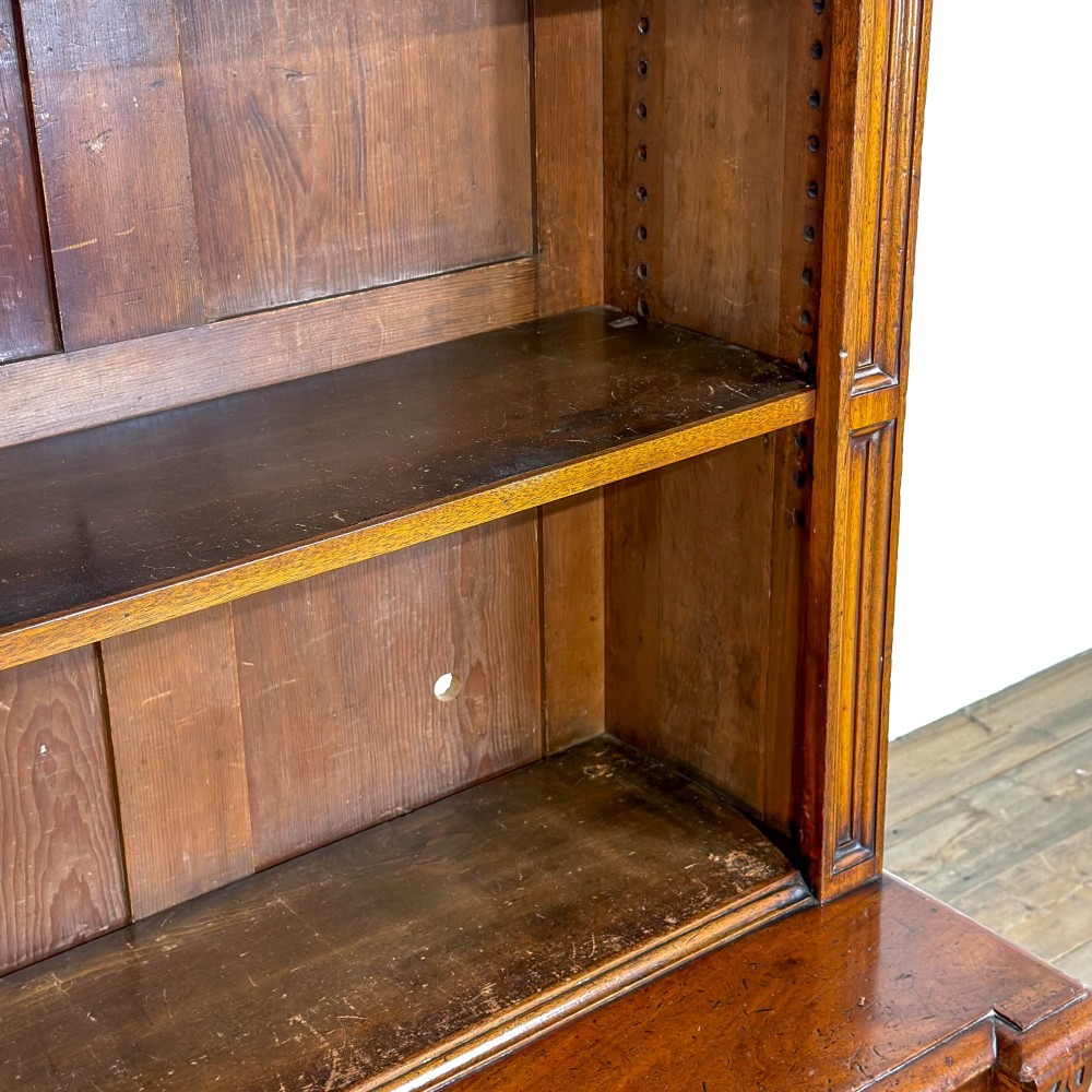 A tall antique open bookcase crafted from warm brown walnut featuring multiple open shelves, fluted side pilasters, and two lower drawers with brass drop handles. View V