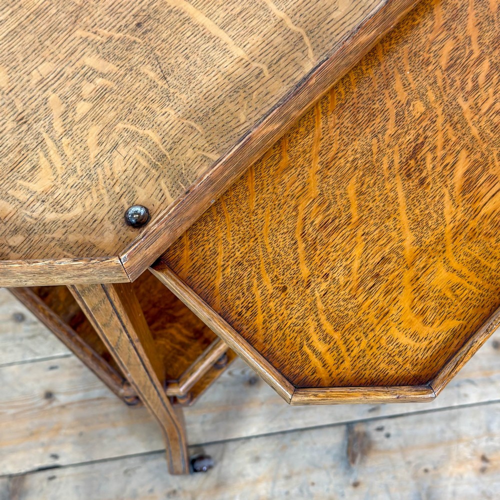 An Edwardian medium oak two-tier tea trolley featuring drop-leaf side panels, a spindle-turned gallery on the lower shelf, and brass castors. View VII