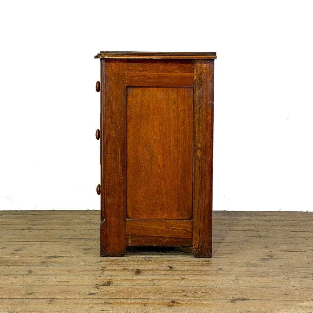 A three-drawer Victorian mahogany chest featuring turned wooden knobs and brass keyhole escutcheons set on a plinth base. View IV