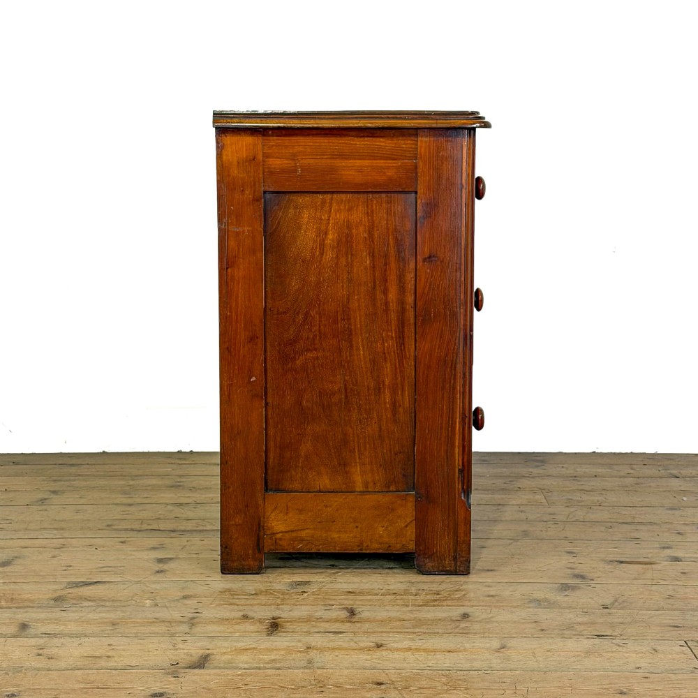 A three-drawer Victorian mahogany chest featuring turned wooden knobs and brass keyhole escutcheons set on a plinth base. View VI