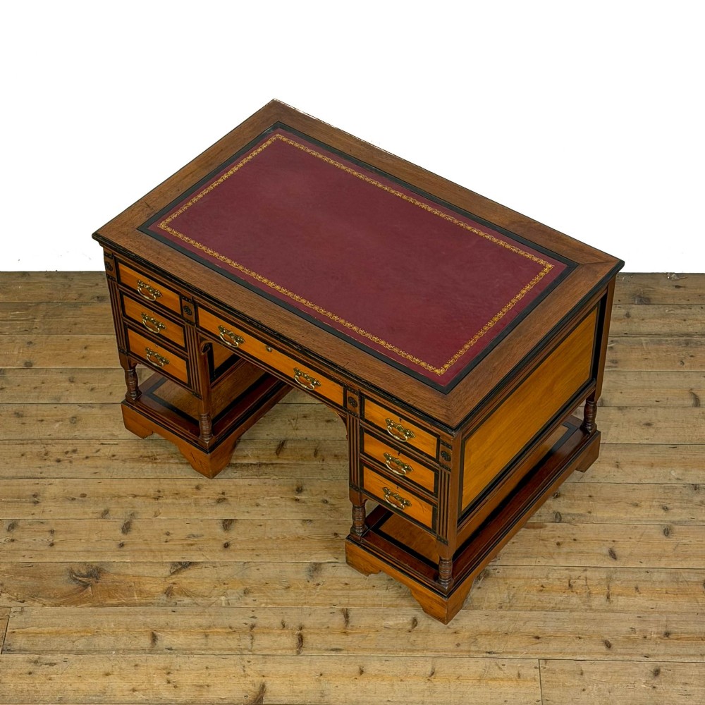 An Aesthetic Movement double-sided partners desk crafted from warm brown wood with black ebonised mouldings, brass drop handles, central kneehole drawer, twin pedestals, open lower shelves, and turned columns. View III