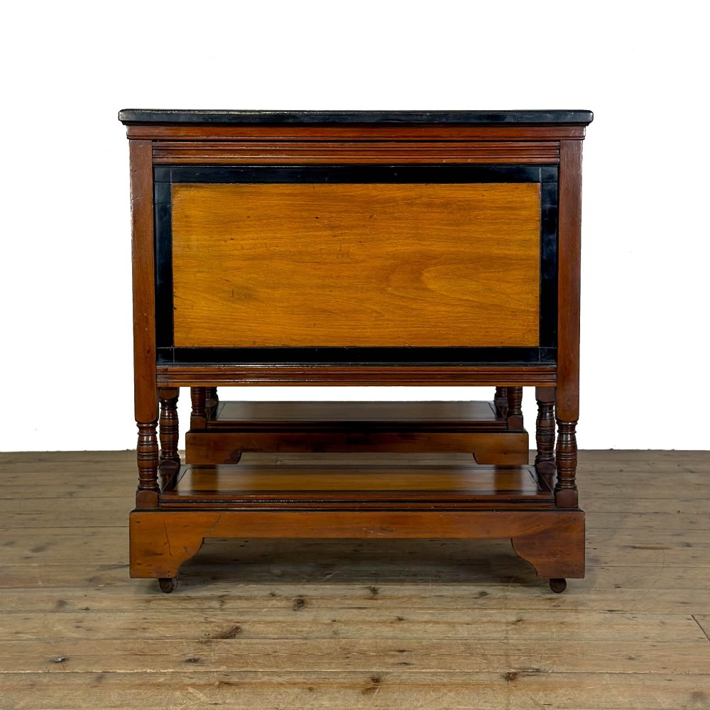 An Aesthetic Movement double-sided partners desk crafted from warm brown wood with black ebonised mouldings, brass drop handles, central kneehole drawer, twin pedestals, open lower shelves, and turned columns. View V