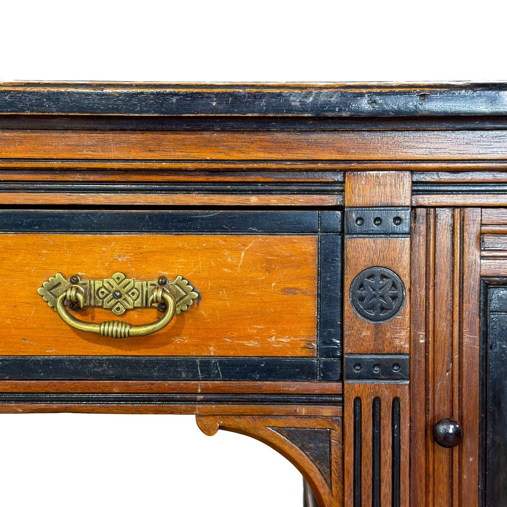 An Aesthetic Movement double-sided partners desk crafted from warm brown wood with black ebonised mouldings, brass drop handles, central kneehole drawer, twin pedestals, open lower shelves, and turned columns. View VIII