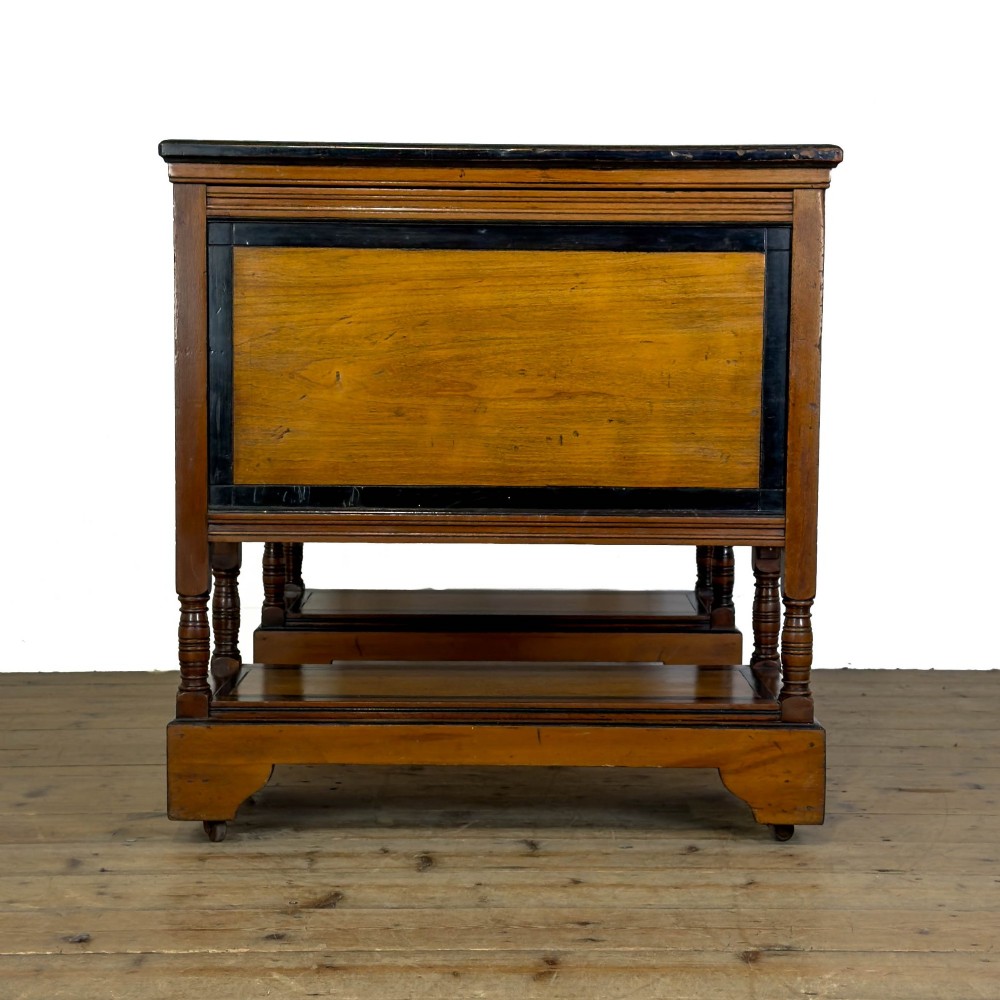 An Aesthetic Movement double-sided partners desk crafted from warm brown wood with black ebonised mouldings, brass drop handles, central kneehole drawer, twin pedestals, open lower shelves, and turned columns. View IX