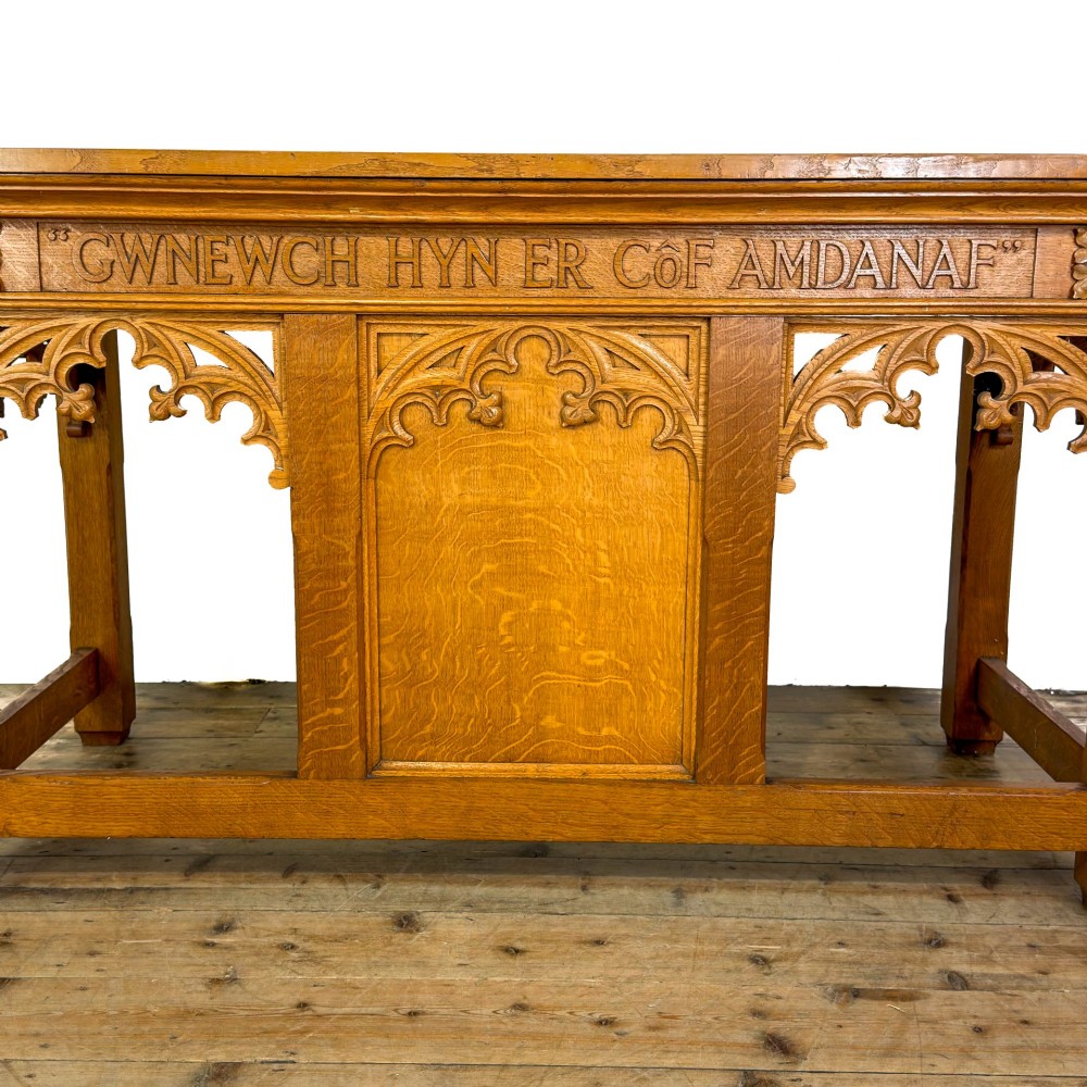 A carved oak Gothic Revival chapel altar table featuring trefoil tracery, an inscribed apron in Welsh script, and a solid rectangular top. View VIII