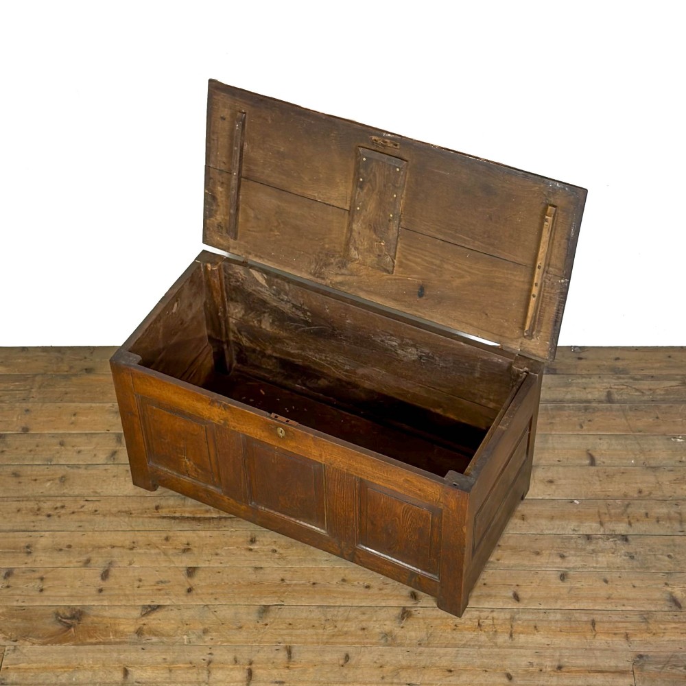 A 19th-century warm brown oak coffer featuring three fielded front panels, a brass keyhole escutcheon, and a flat hinged top lid. View V